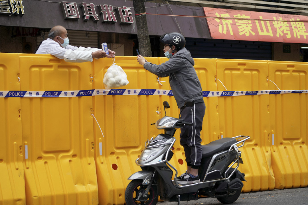 2022年3月30日，中國上海，一名站在機車上的男子越過封鎖區路障掃描二維碼，向商販購買食物。